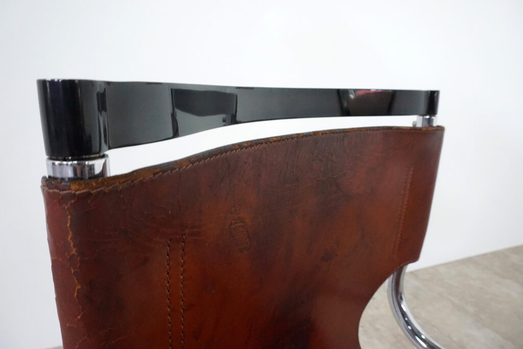 1970年代イタリア人デザイナー カルロ・バルトリ（Carlo Bartoli）によってデザインされたダイニングチェア。背もたれのアルミパーツが破損の為、より強度のあるスチール（黒クロームメッキ）を製作。深みのあるエイジングレザーと、滑らかにカーブする金属フレーム。クラシックとモダンが絶妙に交わる、スタイリッシュなダイニングチェア。背もたれ上部寄り