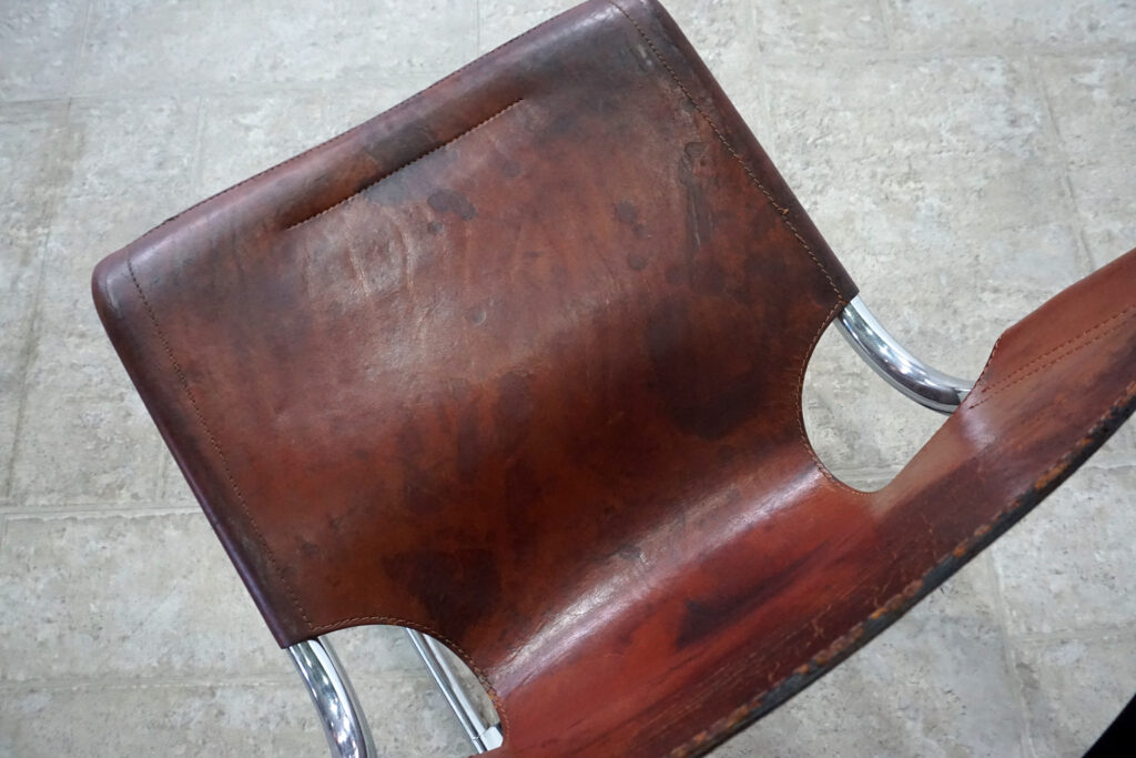 1970年代イタリア人デザイナー カルロ・バルトリ（Carlo Bartoli）によってデザインされたダイニングチェア。背もたれのアルミパーツが破損の為、より強度のあるスチール（黒クロームメッキ）を製作。深みのあるエイジングレザーと、滑らかにカーブする金属フレーム。クラシックとモダンが絶妙に交わる、スタイリッシュなダイニングチェア。座面上部寄り