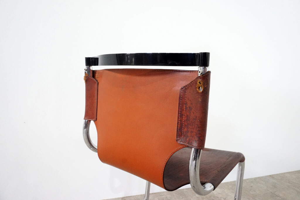 1970年代イタリア人デザイナー カルロ・バルトリ（Carlo Bartoli）によってデザインされたダイニングチェア。背もたれのアルミパーツが破損の為、より強度のあるスチール（黒クロームメッキ）を製作。深みのあるエイジングレザーと、滑らかにカーブする金属フレーム。クラシックとモダンが絶妙に交わる、スタイリッシュなダイニングチェア。背もたれ引き