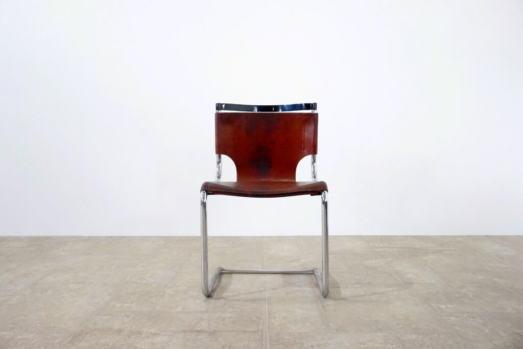 1970年代イタリア人デザイナー カルロ・バルトリ（Carlo Bartoli）によってデザインされたダイニングチェア。背もたれのアルミパーツが破損の為、より強度のあるスチール（黒クロームメッキ）を製作。深みのあるエイジングレザーと、滑らかにカーブする金属フレーム。クラシックとモダンが絶妙に交わる、スタイリッシュなダイニングチェア。正面