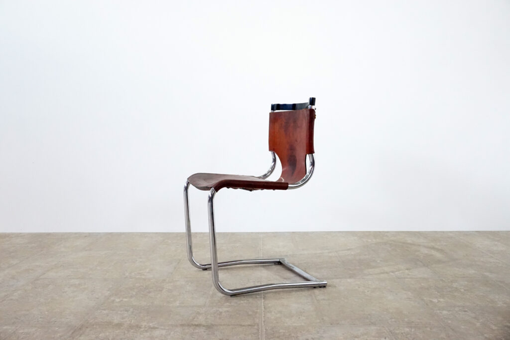 1970年代イタリア人デザイナー カルロ・バルトリ（Carlo Bartoli）によってデザインされたダイニングチェア。背もたれのアルミパーツが破損の為、より強度のあるスチール（黒クロームメッキ）を製作。深みのあるエイジングレザーと、滑らかにカーブする金属フレーム。クラシックとモダンが絶妙に交わる、スタイリッシュなダイニングチェア。左斜め横