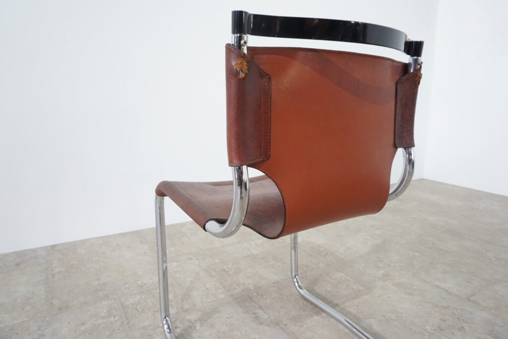 1970年代イタリア人デザイナー カルロ・バルトリ（Carlo Bartoli）によってデザインされたダイニングチェア。背もたれのアルミパーツが破損の為、より強度のあるスチール（黒クロームメッキ）を製作。深みのあるエイジングレザーと、滑らかにカーブする金属フレーム。クラシックとモダンが絶妙に交わる、スタイリッシュなダイニングチェア。背もたれ背面左