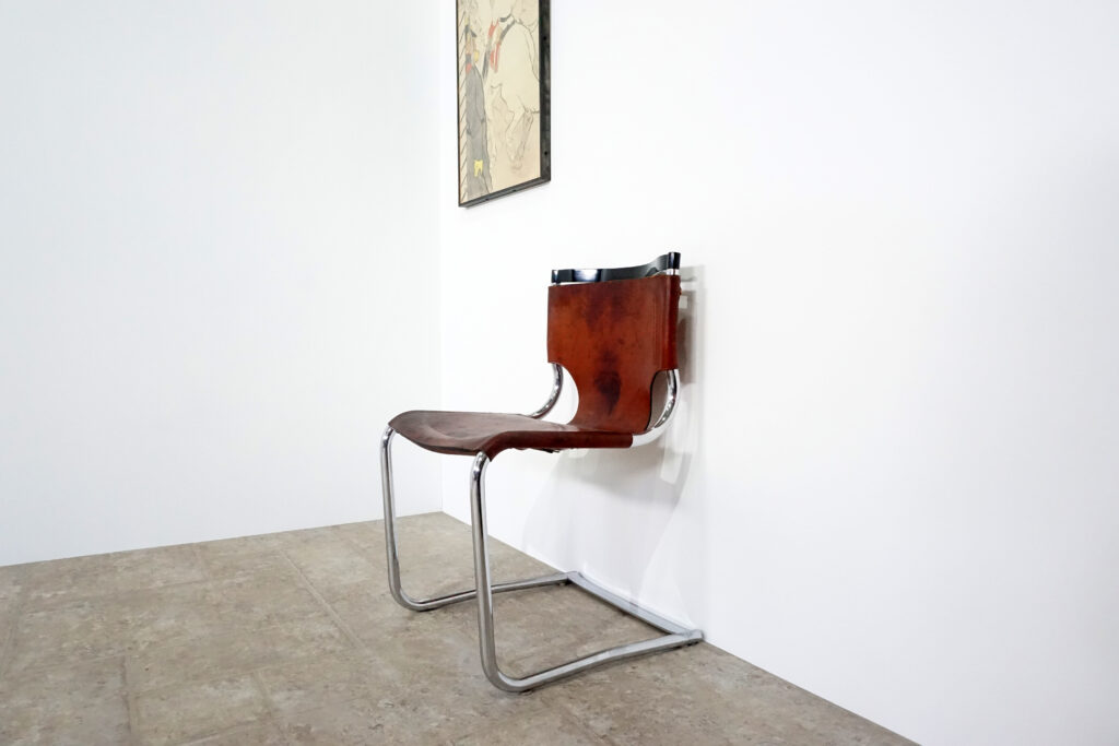 1970年代イタリア人デザイナー カルロ・バルトリ（Carlo Bartoli）によってデザインされたダイニングチェア。背もたれのアルミパーツが破損の為、より強度のあるスチール（黒クロームメッキ）を製作。深みのあるエイジングレザーと、滑らかにカーブする金属フレーム。クラシックとモダンが絶妙に交わる、スタイリッシュなダイニングチェア。背もたれ背面左