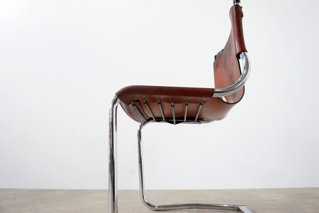 1970年代イタリア人デザイナー カルロ・バルトリ（Carlo Bartoli）によってデザインされたダイニングチェア。背もたれのアルミパーツが破損の為、より強度のあるスチール（黒クロームメッキ）を製作。深みのあるエイジングレザーと、滑らかにカーブする金属フレーム。クラシックとモダンが絶妙に交わる、スタイリッシュなダイニングチェア。座面下部左