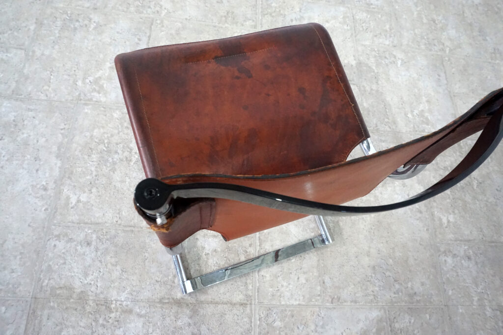 1970年代イタリア人デザイナー カルロ・バルトリ（Carlo Bartoli）によってデザインされたダイニングチェア。背もたれのアルミパーツが破損の為、より強度のあるスチール（黒クロームメッキ）を製作。深みのあるエイジングレザーと、滑らかにカーブする金属フレーム。クラシックとモダンが絶妙に交わる、スタイリッシュなダイニングチェア。座面上部