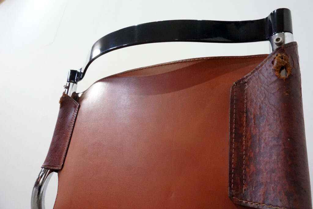 1970年代イタリア人デザイナー カルロ・バルトリ（Carlo Bartoli）によってデザインされたダイニングチェア。背もたれのアルミパーツが破損の為、より強度のあるスチール（黒クロームメッキ）を製作。深みのあるエイジングレザーと、滑らかにカーブする金属フレーム。クラシックとモダンが絶妙に交わる、スタイリッシュなダイニングチェア。背もたれ背面寄り