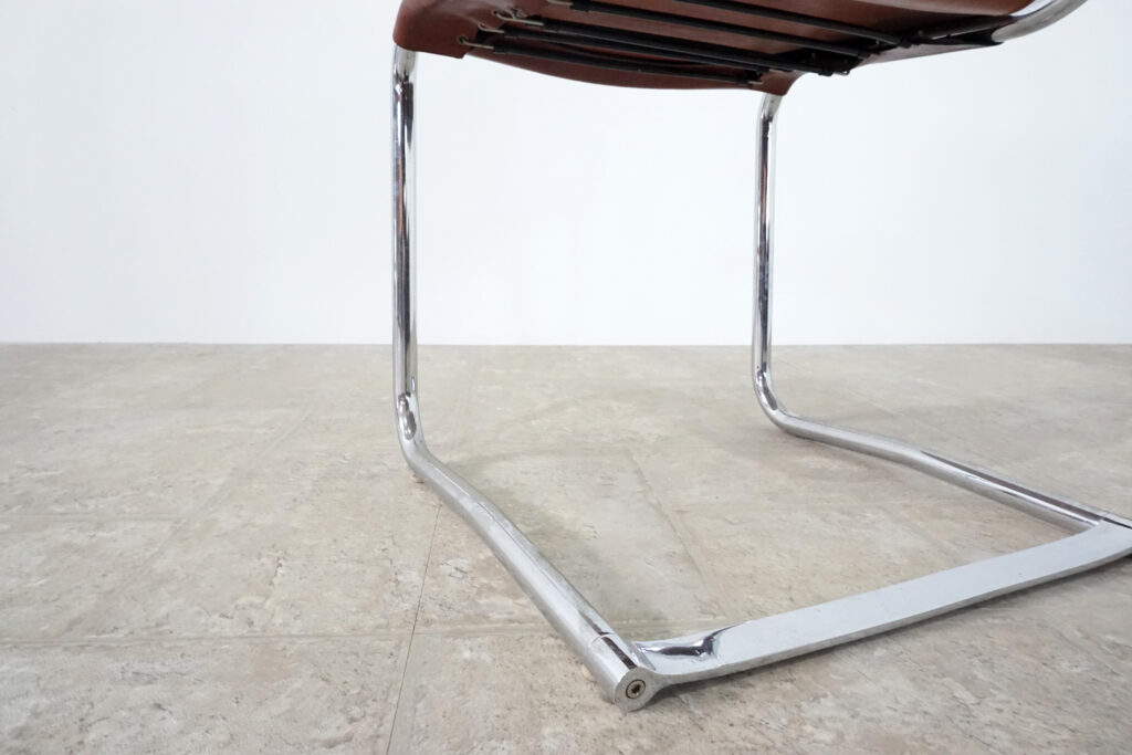 1970年代イタリア人デザイナー カルロ・バルトリ（Carlo Bartoli）によってデザインされたダイニングチェア。背もたれのアルミパーツが破損の為、より強度のあるスチール（黒クロームメッキ）を製作。深みのあるエイジングレザーと、滑らかにカーブする金属フレーム。クラシックとモダンが絶妙に交わる、スタイリッシュなダイニングチェア。足元後ろ