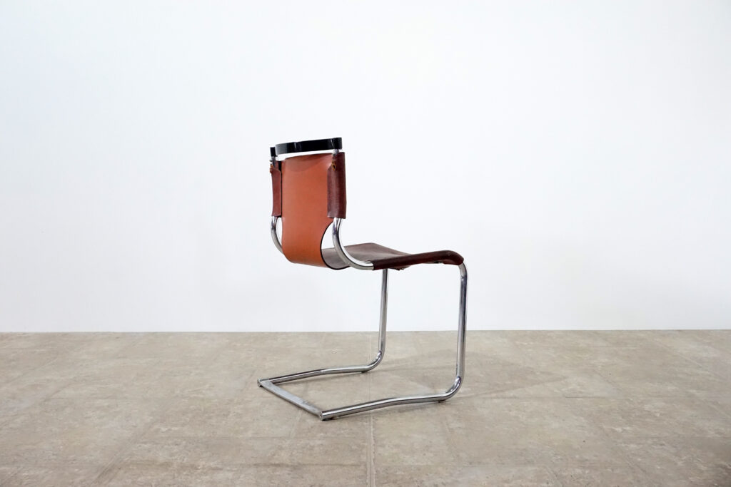 1970年代イタリア人デザイナー カルロ・バルトリ（Carlo Bartoli）によってデザインされたダイニングチェア。背もたれのアルミパーツが破損の為、より強度のあるスチール（黒クロームメッキ）を製作。深みのあるエイジングレザーと、滑らかにカーブする金属フレーム。クラシックとモダンが絶妙に交わる、スタイリッシュなダイニングチェア。右斜め後ろ