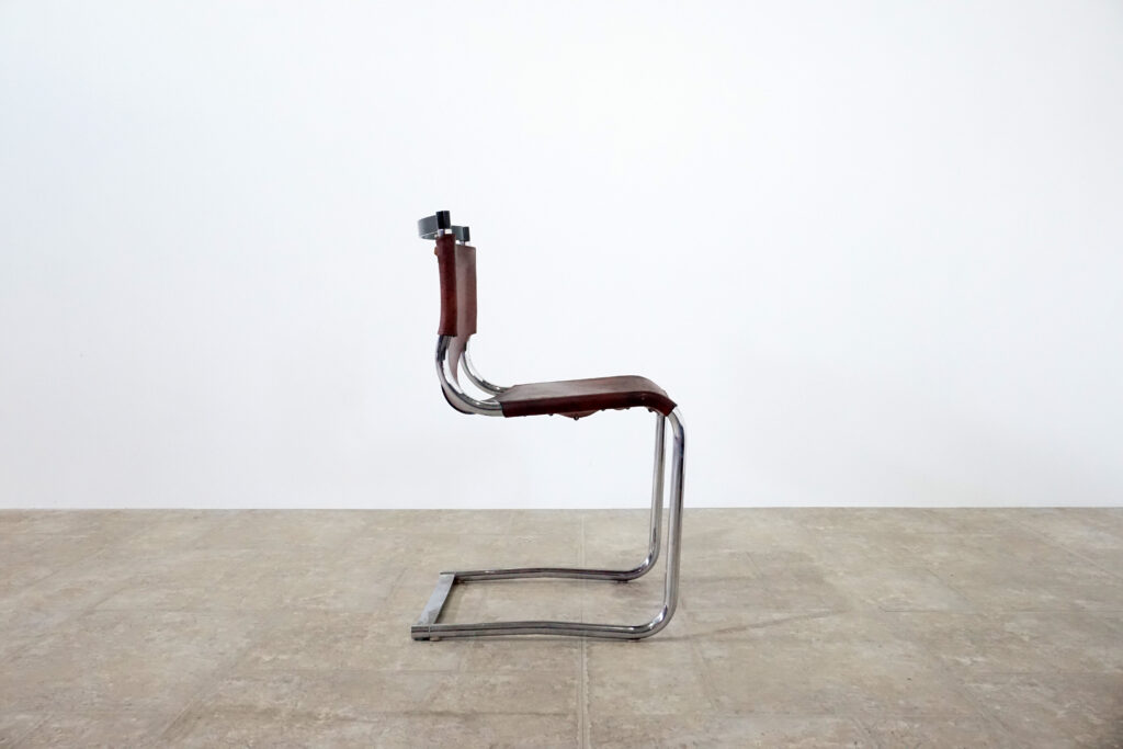 1970年代イタリア人デザイナー カルロ・バルトリ（Carlo Bartoli）によってデザインされたダイニングチェア。背もたれのアルミパーツが破損の為、より強度のあるスチール（黒クロームメッキ）を製作。深みのあるエイジングレザーと、滑らかにカーブする金属フレーム。クラシックとモダンが絶妙に交わる、スタイリッシュなダイニングチェア。右横