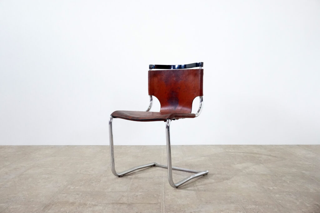 1970年代イタリア人デザイナー カルロ・バルトリ（Carlo Bartoli）によってデザインされたダイニングチェア。背もたれのアルミパーツが破損の為、より強度のあるスチール（黒クロームメッキ）を製作。深みのあるエイジングレザーと、滑らかにカーブする金属フレーム。クラシックとモダンが絶妙に交わる、スタイリッシュなダイニングチェア。メイン