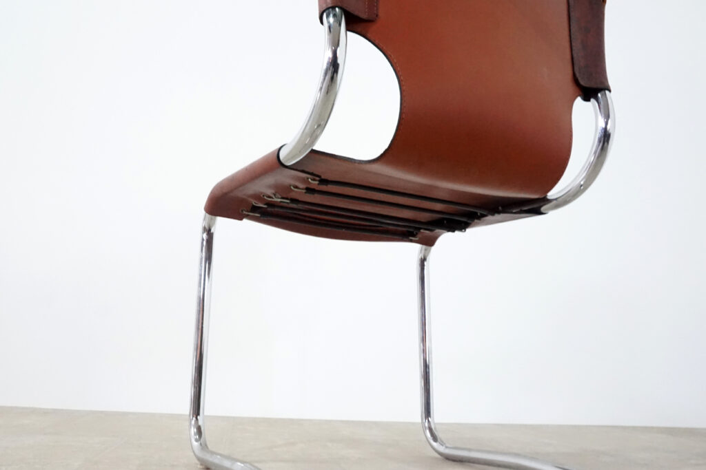 1970年代イタリア人デザイナー カルロ・バルトリ（Carlo Bartoli）によってデザインされたダイニングチェア。背もたれのアルミパーツが破損の為、より強度のあるスチール（黒クロームメッキ）を製作。深みのあるエイジングレザーと、滑らかにカーブする金属フレーム。クラシックとモダンが絶妙に交わる、スタイリッシュなダイニングチェア。背面見上げ