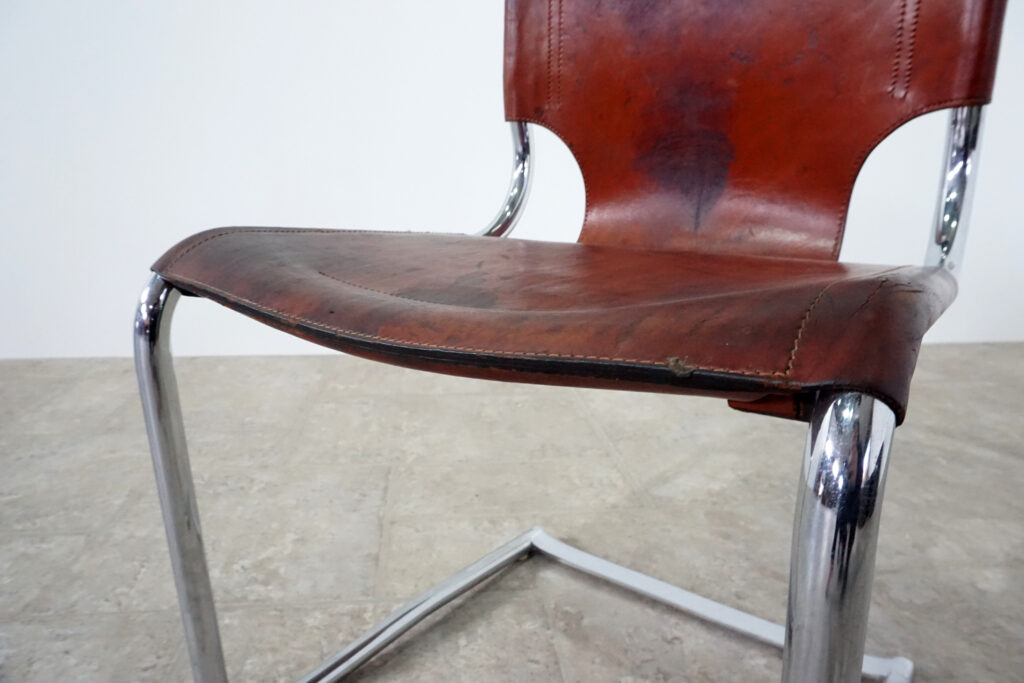 1970年代イタリア人デザイナー カルロ・バルトリ（Carlo Bartoli）によってデザインされたダイニングチェア。背もたれのアルミパーツが破損の為、より強度のあるスチール（黒クロームメッキ）を製作。深みのあるエイジングレザーと、滑らかにカーブする金属フレーム。クラシックとモダンが絶妙に交わる、スタイリッシュなダイニングチェア。座面左前