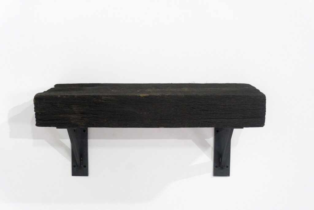 古材の梁から切り出した厚みのある木塊を、そのまま棚として再構成したウォールシェルフ。時間を刻んだ木材の質感と重量感を活かし、壁面から静かに突き出すような存在感をつくります。棚受けには、鉄の黒皮材を用いたオリジナルブラケットを新規制作。素材の表情を残した黒皮鉄を黒塗装で仕上げ、古材の力強さと調和するシンプルな構造としています。古材が持つ個体差や痕跡をそのまま活かしながら、現代の空間に静かな緊張感を与えるプロダクトです。正面上部