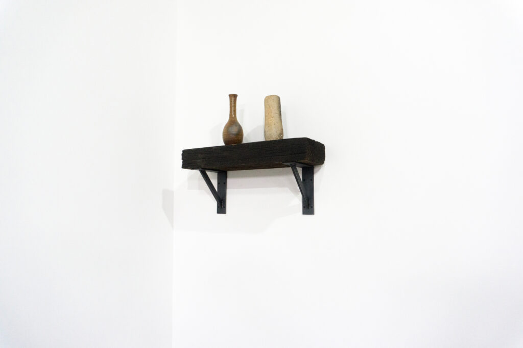 古材の梁から切り出した厚みのある木塊を、そのまま棚として再構成したウォールシェルフ。時間を刻んだ木材の質感と重量感を活かし、壁面から静かに突き出すような存在感をつくります。棚受けには、鉄の黒皮材を用いたオリジナルブラケットを新規制作。素材の表情を残した黒皮鉄を黒塗装で仕上げ、古材の力強さと調和するシンプルな構造としています。古材が持つ個体差や痕跡をそのまま活かしながら、現代の空間に静かな緊張感を与えるプロダクトです。メイン