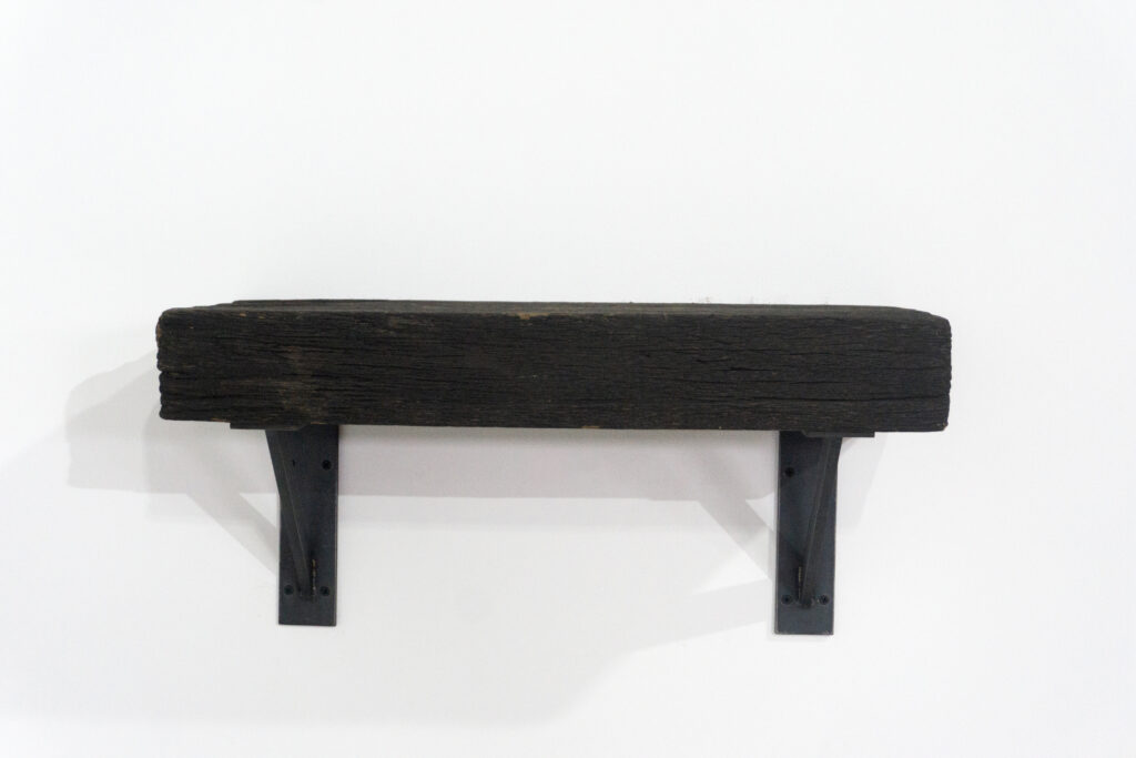 古材の梁から切り出した厚みのある木塊を、そのまま棚として再構成したウォールシェルフ。時間を刻んだ木材の質感と重量感を活かし、壁面から静かに突き出すような存在感をつくります。棚受けには、鉄の黒皮材を用いたオリジナルブラケットを新規制作。素材の表情を残した黒皮鉄を黒塗装で仕上げ、古材の力強さと調和するシンプルな構造としています。古材が持つ個体差や痕跡をそのまま活かしながら、現代の空間に静かな緊張感を与えるプロダクトです。正面寄り