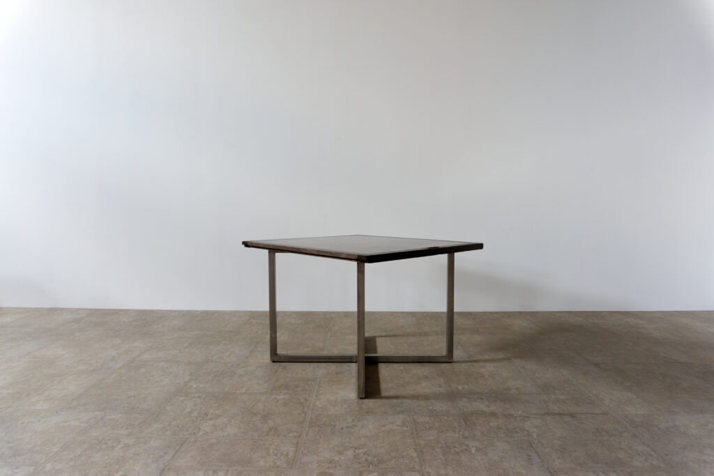 古い木製扉を再利用したテーブル。既存の木枠はそのまま活かし、中央にはステンレス板をフラットに納めています。天板は段差を抑えた構成で、実用性と意匠性を両立。脚部にはステンレス角パイプを使用し、十分な強度と安定性を確保。木部の経年変化とステンレスの均質な質感が対比され、空間に適度な緊張感を与える。一点ごとに表情の異なる木枠を使用しているため、同一仕様でも個体差があります。住宅空間から店舗什器まで幅広く使用可能。Threshold / Plane 01斜め