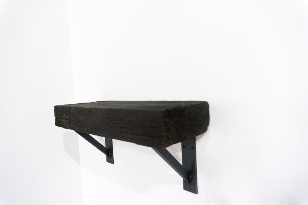 古材の梁から切り出した厚みのある木塊を、そのまま棚として再構成したウォールシェルフ。時間を刻んだ木材の質感と重量感を活かし、壁面から静かに突き出すような存在感をつくります。棚受けには、鉄の黒皮材を用いたオリジナルブラケットを新規制作。素材の表情を残した黒皮鉄を黒塗装で仕上げ、古材の力強さと調和するシンプルな構造としています。古材が持つ個体差や痕跡をそのまま活かしながら、現代の空間に静かな緊張感を与えるプロダクトです。サイド