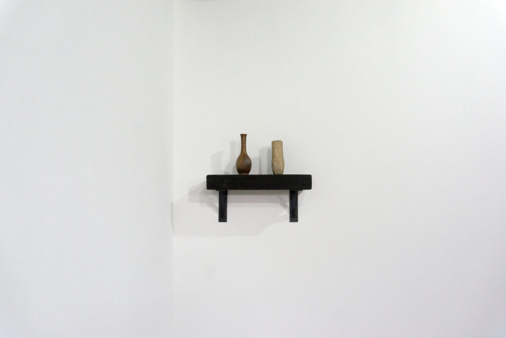 古材の梁から切り出した厚みのある木塊を、そのまま棚として再構成したウォールシェルフ。時間を刻んだ木材の質感と重量感を活かし、壁面から静かに突き出すような存在感をつくります。棚受けには、鉄の黒皮材を用いたオリジナルブラケットを新規制作。素材の表情を残した黒皮鉄を黒塗装で仕上げ、古材の力強さと調和するシンプルな構造としています。古材が持つ個体差や痕跡をそのまま活かしながら、現代の空間に静かな緊張感を与えるプロダクトです。正面
