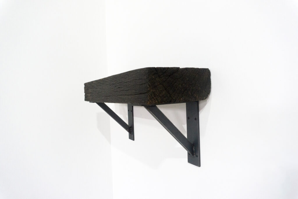 古材の梁から切り出した厚みのある木塊を、そのまま棚として再構成したウォールシェルフ。時間を刻んだ木材の質感と重量感を活かし、壁面から静かに突き出すような存在感をつくります。棚受けには、鉄の黒皮材を用いたオリジナルブラケットを新規制作。素材の表情を残した黒皮鉄を黒塗装で仕上げ、古材の力強さと調和するシンプルな構造としています。古材が持つ個体差や痕跡をそのまま活かしながら、現代の空間に静かな緊張感を与えるプロダクトです。真横